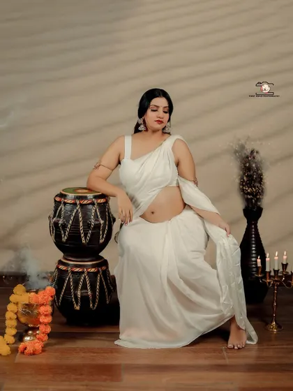 This portrait showcases the mother-to-be in a serene and powerful pose. She leans against traditional Indian drums (tabla), her white saree and exposed baby bump creating a look that is both artistic and culturally rooted.
