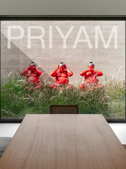 Three bright red sumo wrestler sculptures sit playfully among ornamental grasses. This installation, viewed from a dining room window, adds a bold pop of color and character to the minimalist landscape.