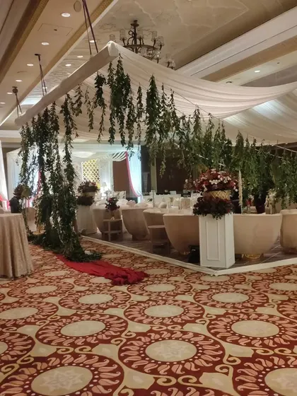 This image shows a VIP dining area within a large banquet hall. The space is defined by a canopy with hanging greenery, creating an exclusive and beautifully decorated section for close family.