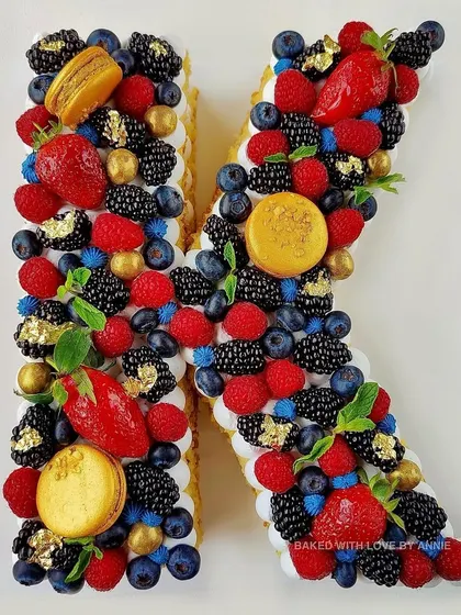 Another custom monogram cake, this time the letter 'K', adorned with fresh berries, macarons, and touches of gold leaf.