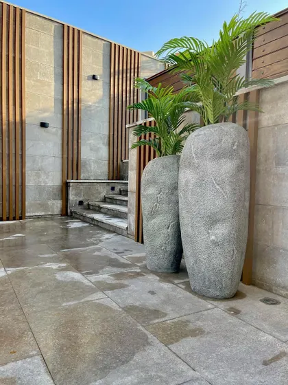Tall, modern planters add vertical interest to this patio space. The textured grey finish of the planters complements the stone paving and the wood-slatted feature wall.
