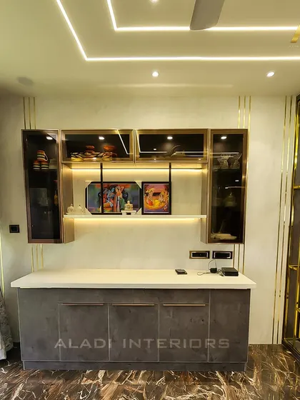 A modern crockery unit with a grey countertop and backlit glass cabinets. The gold-finished metal partition adds a touch of glamour and separates the space elegantly.