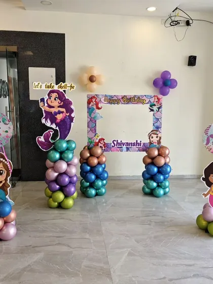 A fun photo booth area with a custom frame and mermaid character cutout's on balloon pillar's.