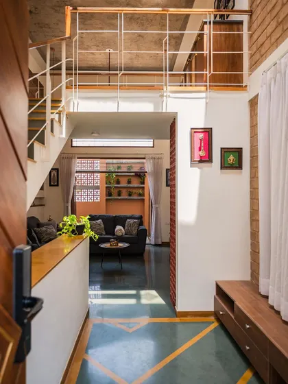 The entrance foyer of the Kaustubha Residence, with inlaid floor patterns leading the eye towards the living area. The view through to the back of the house creates an immediate sense of depth and openness.