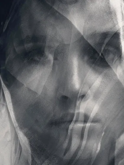 A layered, abstract portrait in black and white. The use of translucent fabric over the face creates a mysterious and thought-provoking image about perception and hidden emotions.