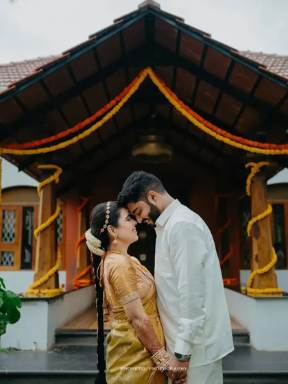A classic romantic pose, with the couple touching foreheads in front of a traditionally decorated house.