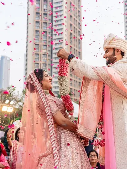A beautiful, happy moment during the varmala exchange, with both bride and groom smiling as petals rain down on them.