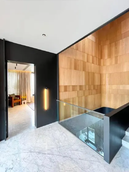 This corridor uses a dynamic partition of black metal, glass, and wood to separate the hallway from the staircase. The design creates a visually interesting transition while maintaining a sense of openness.