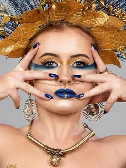 A close-up of the creative headpiece and makeup. The gold and blue tones are vibrant and metallic, creating a look that is both artistic and glamorous.