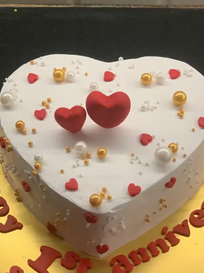 A classic heart-shaped anniversary cake. The simple white cake is decorated with red hearts and gold and white pearls.