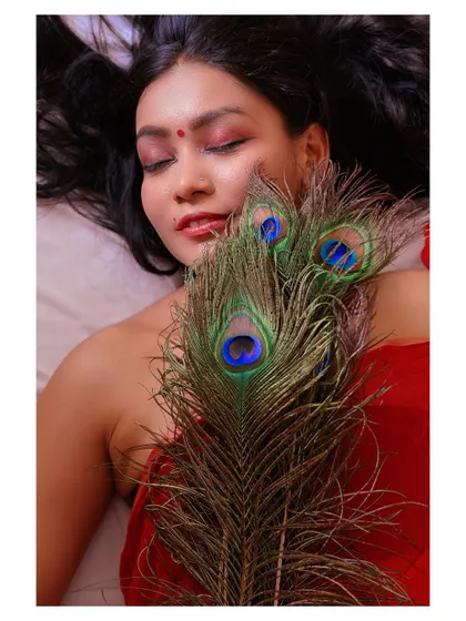 An artistic portrait using a peacock feather as a prop. The model's closed eyes and serene expression create a meditative and beautiful image.