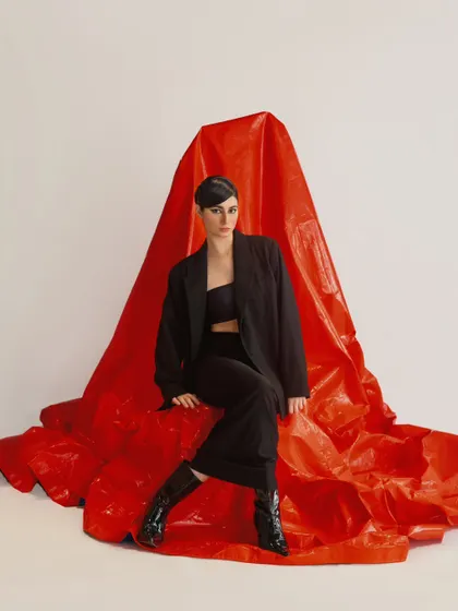 A full-length shot that uses the draped red fabric to create a dramatic, sculptural element. This is a great example of creative art direction in a fashion shoot.