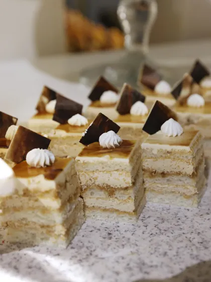 Our layered opera cake, cut into perfect, bite-sized squares. The geometric precision and delicate chocolate work make this a truly elegant and sophisticated dessert choice.
