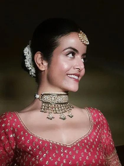 A smiling bride with a classic, clean makeup look and a traditional hair bun adorned with fresh white flowers. This side profile highlights the neatness of the hairstyle and the radiance of her skin.