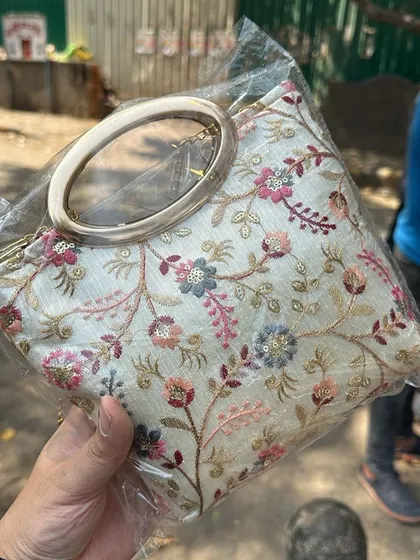 A beautiful white clutch with colourful floral embroidery and a large ring handle. This is a perfect evening bag sourced from a Delhi market.
