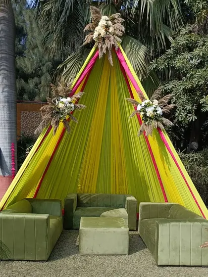 A modern and chic lounge seating area for a Mehendi. The tent-like draping in yellow and pink, combined with plush olive green sofas, creates a comfortable and stylish space for guests to relax.