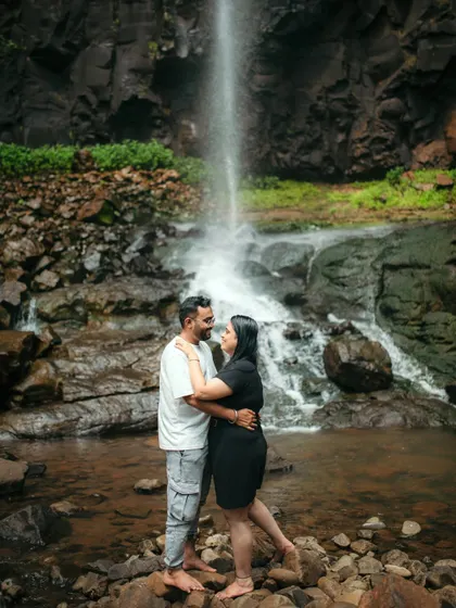 A couple embraces in front of a majestic waterfall, a perfect example of a dramatic pre-wedding location.