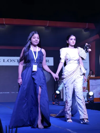 A student designer walks the ramp with her model, presenting her final creation to the audience.