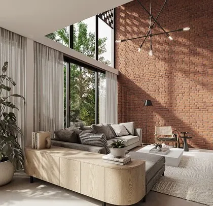 The double-height living room in a Kolgaon villa features a prominent brick wall that continues from the exterior. This design choice emphasizes the material connection between the architecture and the interiors, creating a cohesive and earthy feel.