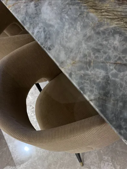 An overhead shot of a dining chair with beige corduroy upholstery next to a grey marble dining table, highlighting the contrast of soft and hard textures.