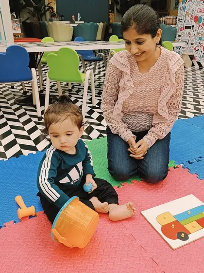 A mother watches as her child plays with a puzzle and a toy drum, showing how we provide a variety of learning tools.