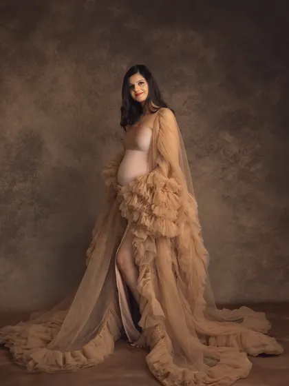 This full-length studio portrait captures the elegance of a flowing nude gown and robe. The mom-to-be's confident pose and happy expression radiate pure maternal glow.