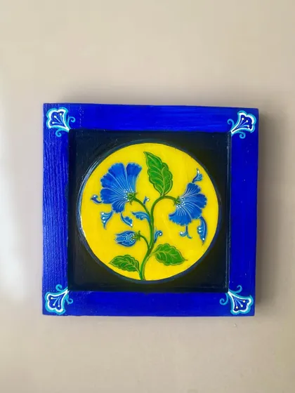 A close-up of the blue-framed piece, inspired by Jaipur blue pottery. The bright yellow background makes the blue flowers pop.