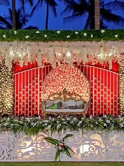 An outdoor stage with a backdrop of red and white flowers against a lush green wall. The ornate white base adds a touch of elegance to this vibrant and natural setting.