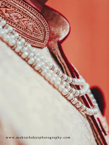 A detail shot of the groom's attire, focusing on the pearl necklace against the rich fabric of his sherwani.