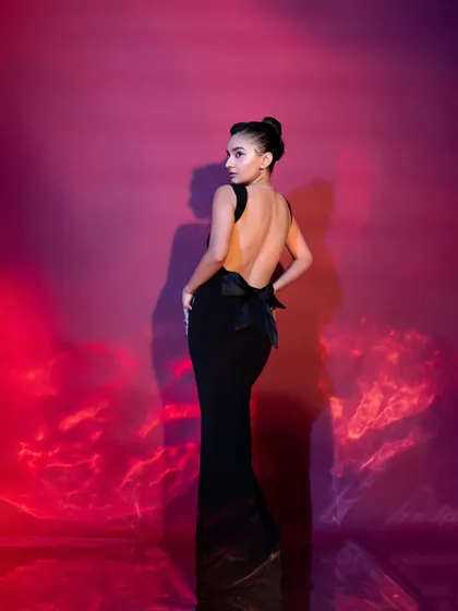 A timeless black gown for Anushka Sen. This look features a dramatic open back with a large bow detail, perfect for making a statement at any formal event or awards night.