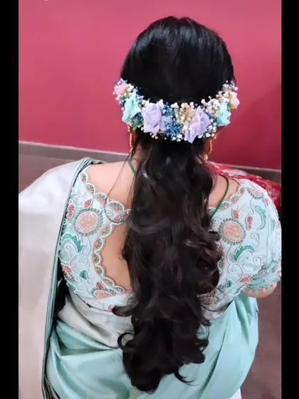 A half-ponytail style with soft curls, adorned with a beautiful pastel-colored floral hairpiece.