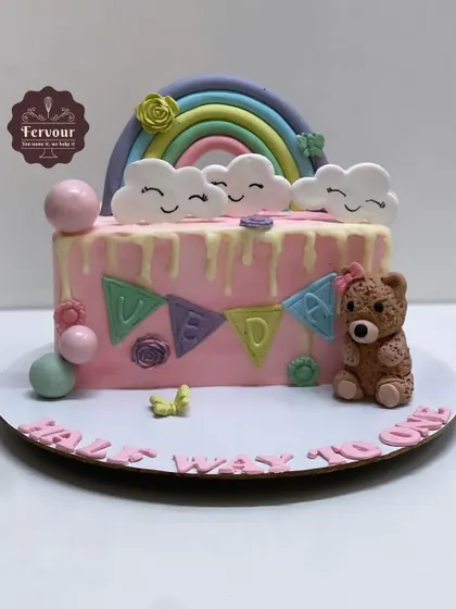 A "Half Way to One" cake celebrating a 6-month milestone. This adorable cake features a rainbow, teddy bear, and pastel-colored decorations.