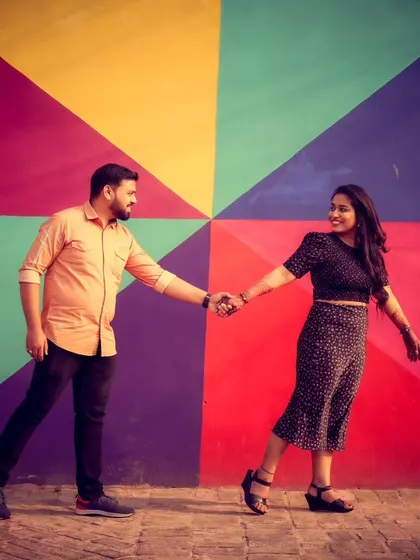 A vibrant and playful pre-wedding photo. The colorful geometric background adds a fun, modern energy to this shot of the couple holding hands.