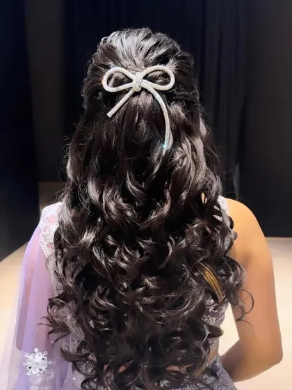 Another angle of this gorgeous open hairstyle with voluminous curls and a chic bow accessory. It's a versatile look that works beautifully with modern lehengas and gowns.