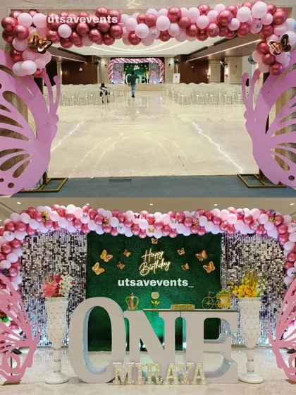 A grand butterfly-themed entrance arch and stage for a first birthday. The setup uses pink butterfly cutouts, a shimmer and grass wall backdrop, and a large 'ONE' sign for a stunning visual impact.
