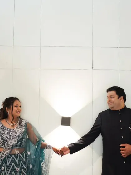A classic engagement portrait, with the couple holding hands against a modern, well-lit backdrop.