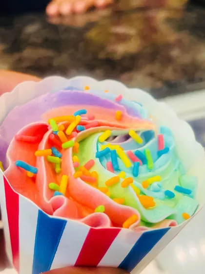 A hand-held shot of a rainbow cupcake, showcasing its vibrant colors in a striped red, white, and blue liner.