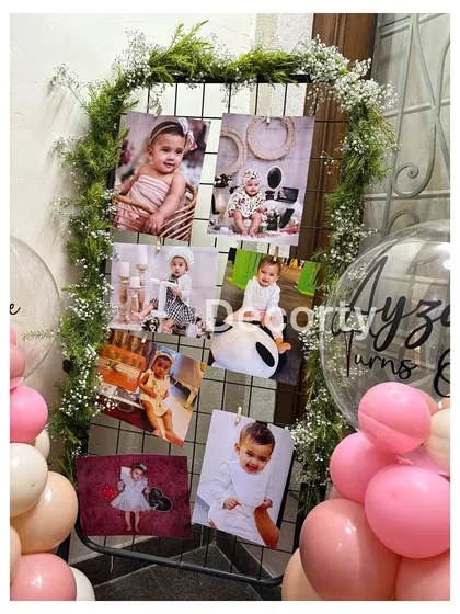 A creative photo display for a butterfly-themed party, using a greenery-adorned grid to hang pictures of the birthday girl's first year.