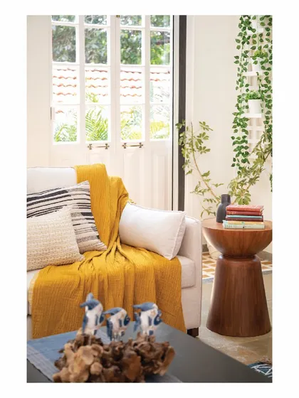 In this Goan villa, we created an intimate corner with a comfortable sofa and a solid wood side table. The use of a bright yellow throw and natural textures makes this an inviting spot to read a book or enjoy the garden view.