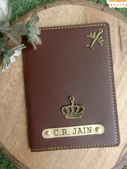 A beautifully styled shot of the personalized passport cover for 'C.R. Jain'. The combination of the crown and airplane charms adds a royal and adventurous touch.