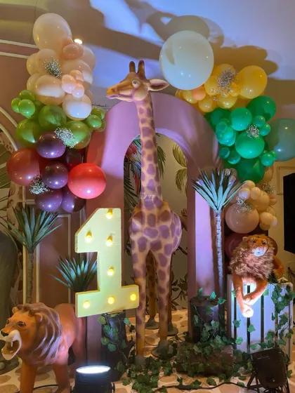 A close-up of the 'Wild One' decor, featuring a lit-up number '1', a tall giraffe, and lions, all framed by a beautiful balloon arrangement.