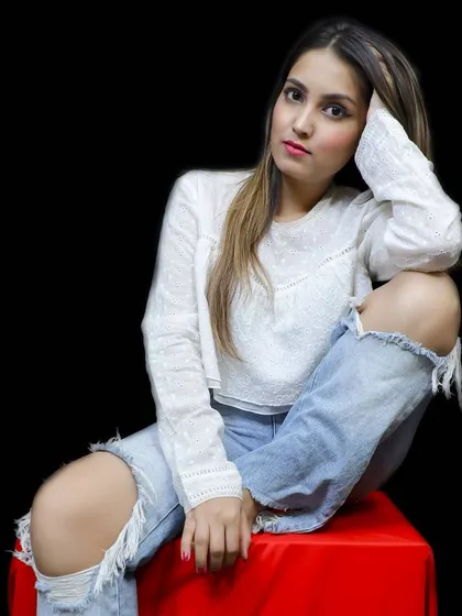 A seated portrait against a stark black background, making the model's white top and ripped jeans pop for a clean portfolio shot.