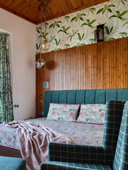 The master bedroom feels like a cozy cabin, with warm timber finishes and a fluted bed back. Lush foliage-print wallpaper and curtains blur the line between indoors and out, making the space feel both grounded and dreamlike.