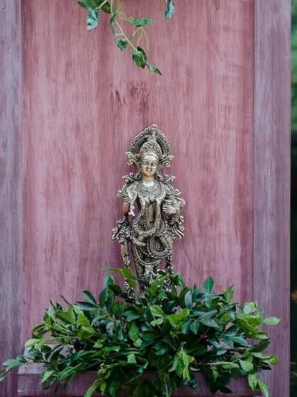 A brass deity placed against a wooden backdrop by the pond, integrating spiritual elements into the decor.
