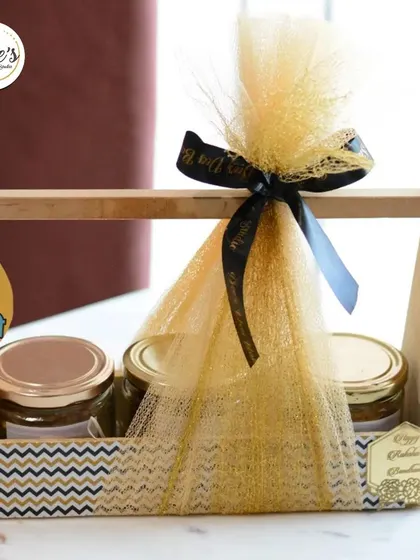 A stylish wooden caddy hamper perfect for Rakhi. This gift set holds three jars of delicious treats and is decorated with a fun "Teri Yaari Sabse Pyaari" tag, celebrating the bond of friendship.