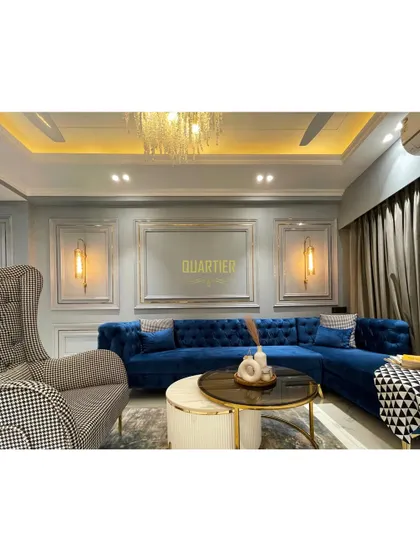 Another angle of the European-inspired living room at Elite Golf Greens. The combination of the tufted blue sofa, houndstooth armchair, and elegant wall mouldings creates a sophisticated and timeless look.