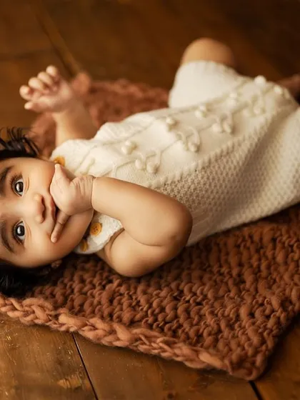 A sweet and expressive baby lying on a textured brown mat. This pose is great for younger sitters who are still mastering tummy time.
