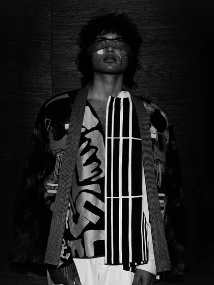 Another dramatic black and white shot, where the model's blindfolded face is partially obscured by shadow. The bold lines and patterns of the clothing stand out, creating a visually complex image.