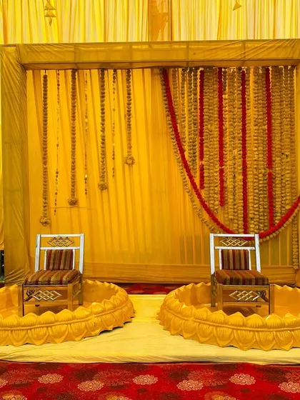 A traditional Haldi seating arrangement with low, lotus-shaped seats and a backdrop of yellow drapes and marigold garlands.