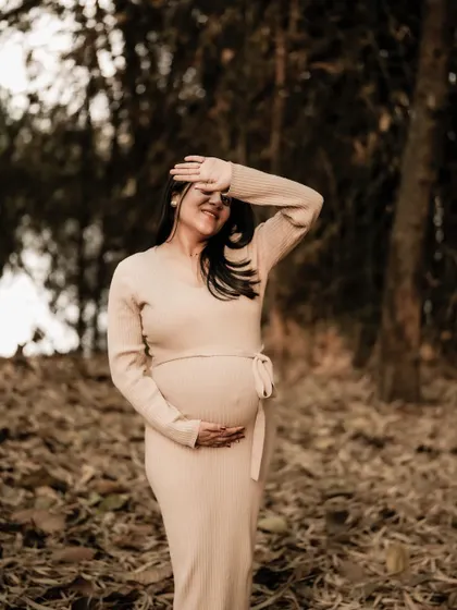 A candid and happy moment in the woods. The mom-to-be shields her eyes from the sun with a smile, basking in the warmth and the moment.